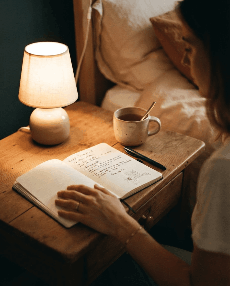 Table de nuit avec une veilleuse allumée et un carnet