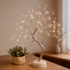 Veilleuse arbre lumineux bonsaï en lumière blanc chaud, branches argentées et base blanche posée sur un meuble